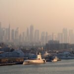 Yachts moored at Dubai Marina with the surrounding high-rise towers behind them in morning haze.