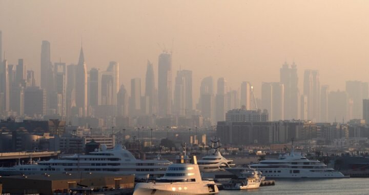 Yachts moored at Dubai Marina with the surrounding high-rise towers behind them in morning haze.