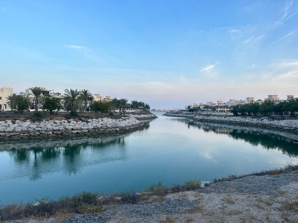 Waterway running through a low-rise residential area in Ras Al Khaimah, lined with palms under a clear sky.