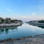 Waterway running through a low-rise residential area in Ras Al Khaimah, lined with palms under a clear sky.