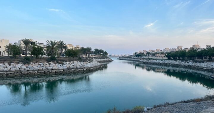 Waterway running through a low-rise residential area in Ras Al Khaimah, lined with palms under a clear sky.