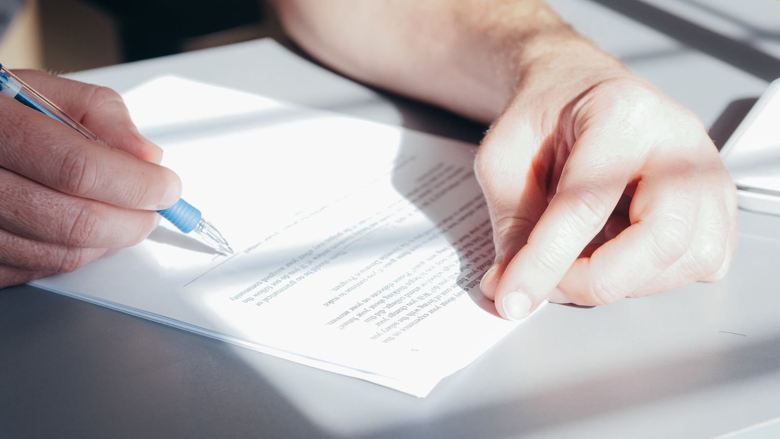 Close-up of a person signing a printed contract with a pen on a desk.