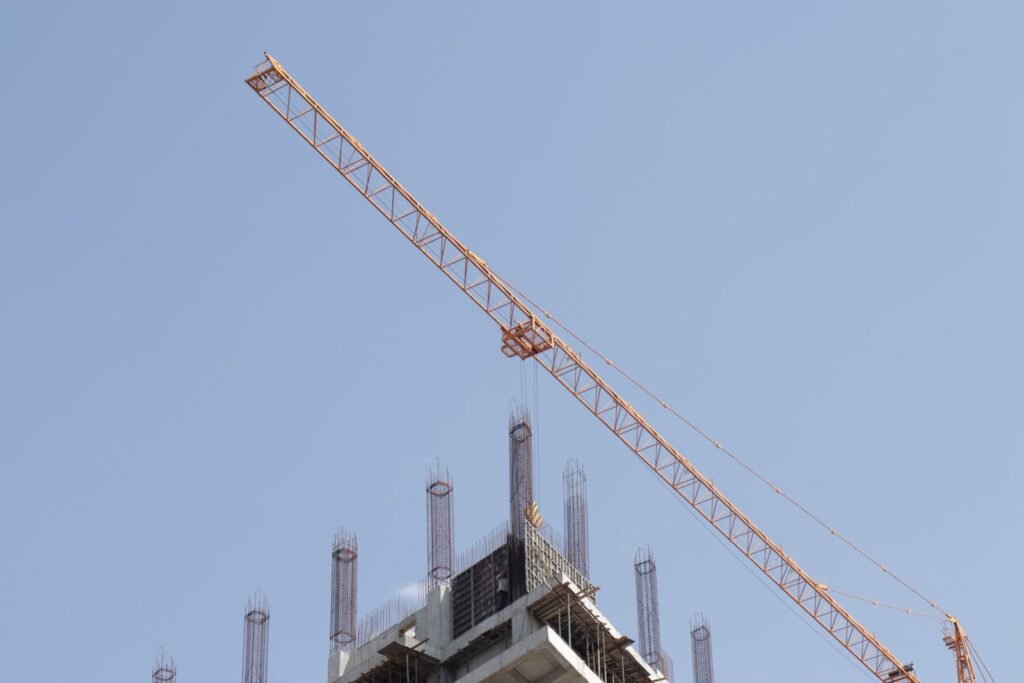 Orange tower crane working above an unfinished high-rise structure against a clear blue sky.