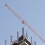 Orange tower crane working above an unfinished high-rise structure against a clear blue sky.