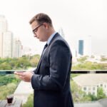 Overseas investor at a laptop with an off-plan brochure and a bank transfer screen, Dubai skyline behind — is it safe to buy property in Dubai as a foreigner?